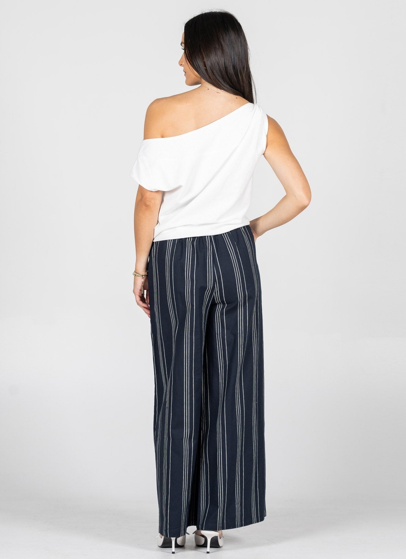 Woman wearing a white off-shoulder top and navy striped pants on a white background