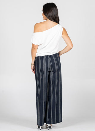 Woman wearing a white off-shoulder top and navy striped pants on a white background