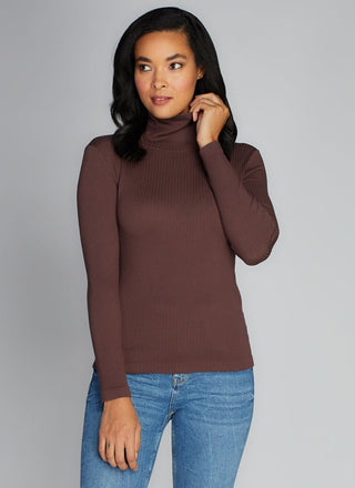 Woman wearing a brown turtleneck sweater and blue jeans against a gray background