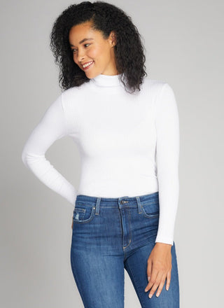 Woman wearing a white turtleneck and blue jeans against a gray background