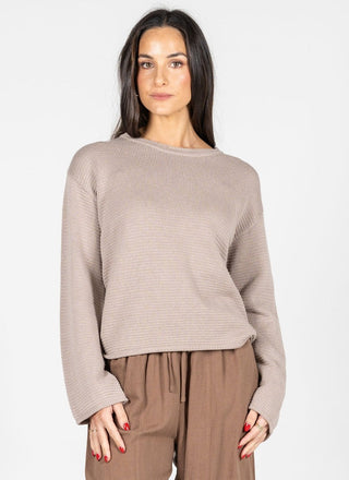 Woman wearing a beige sweater and brown pants on a white background