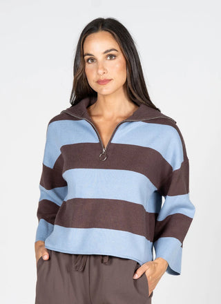A woman modeling a brown and light blue striped quarter-zip pullover sweater with a mock neck, paired with brown drawstring pants, against a light gray studio background.
