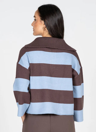 A woman shown from the back wearing a cropped knit sweater with wide horizontal stripes in brown and light blue, paired with brown pants against a plain light gray studio background.