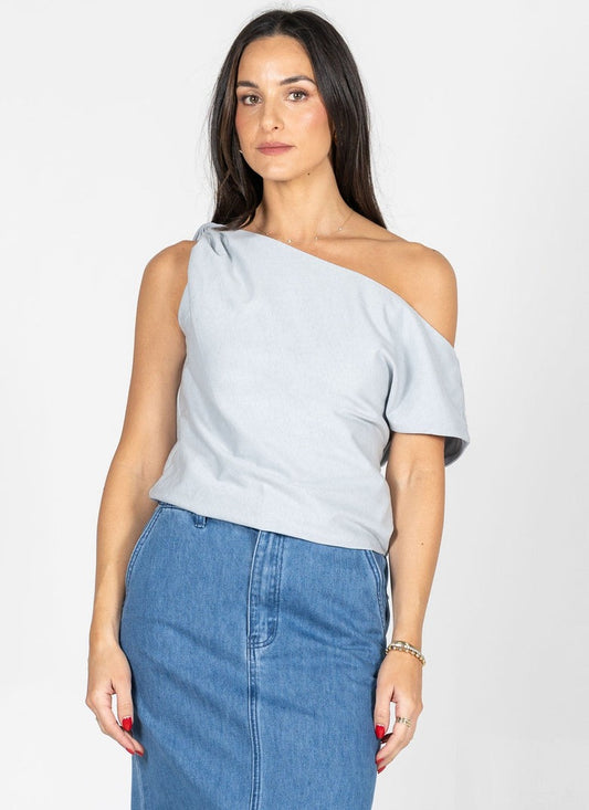 Woman wearing a light gray one-shoulder top and blue jeans on a white background