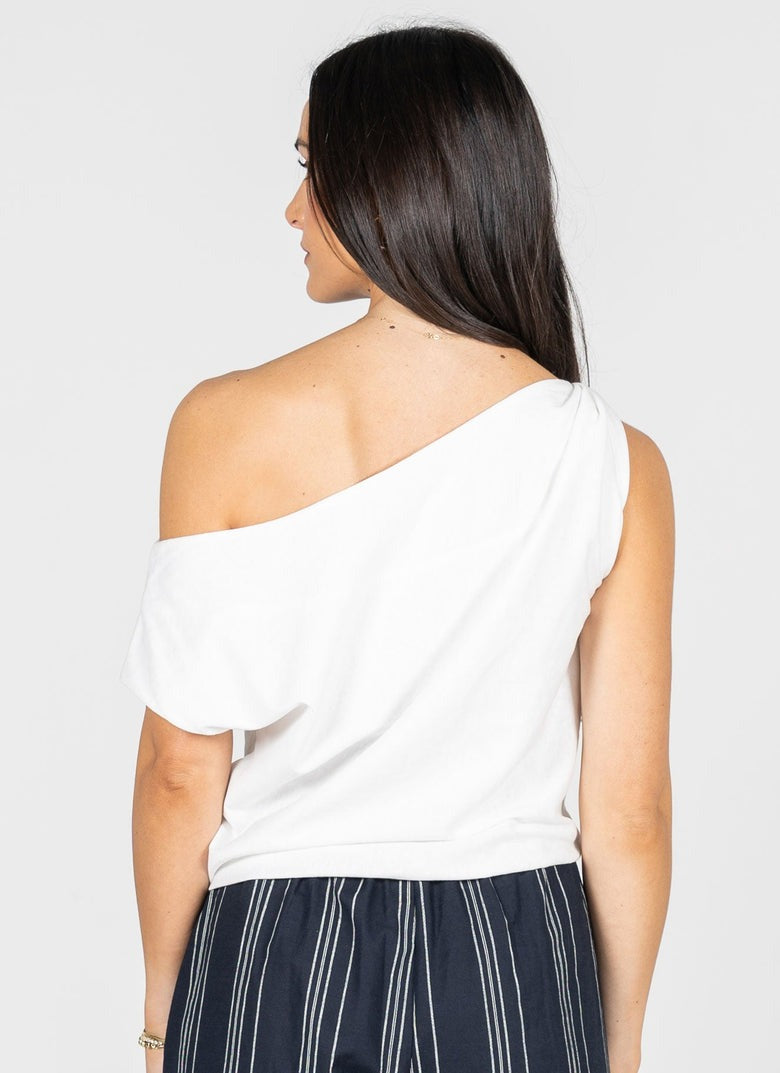 Woman wearing a white off-shoulder top and dark pants on a plain background