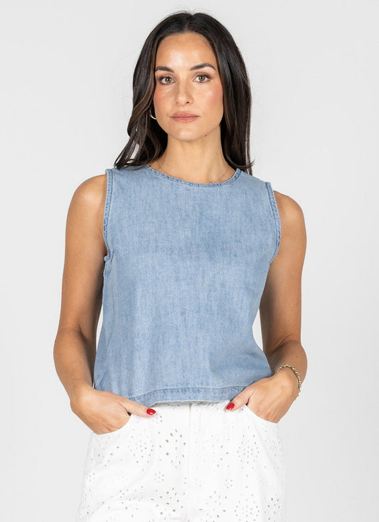 Woman wearing a light blue denim sleeveless top against a white background