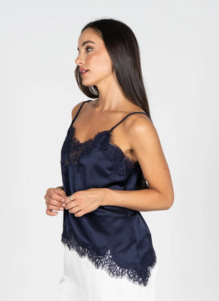 A woman wearing a navy blue satin camisole top with lace trim, shown in profile against a plain light gray studio background.