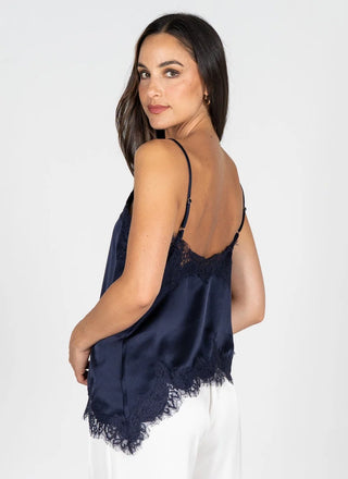 A woman wearing a navy blue satin camisole top with lace trim and thin spaghetti straps, shown from a three-quarters back view against a light gray studio background.