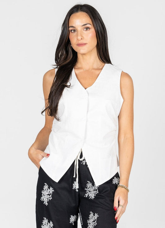 Woman wearing a white sleeveless top and black pants with floral embroidery on a white background