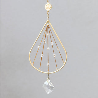 A small gold-colored brass suncatcher with a teardrop shape, featuring clear crystal beads strung along its frame, hanging by a chain.