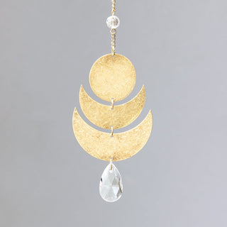 A small brass suncatcher with gold plating, featuring a crescent moon shape and a crystal pendant, hanging from a chain.