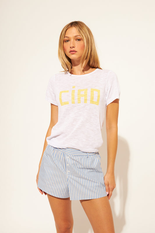 Woman wearing a white t-shirt with 'Ciao' printed in yellow and striped shorts on a plain background