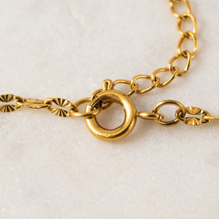Close-up of a gold chain necklace on a textured white background.