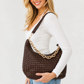Women wearing a brown woven shoulder bag against a neutral photo background. 