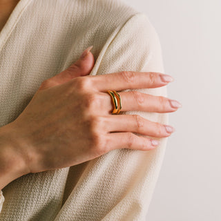 Hand wearing a gold ring on a neutral background