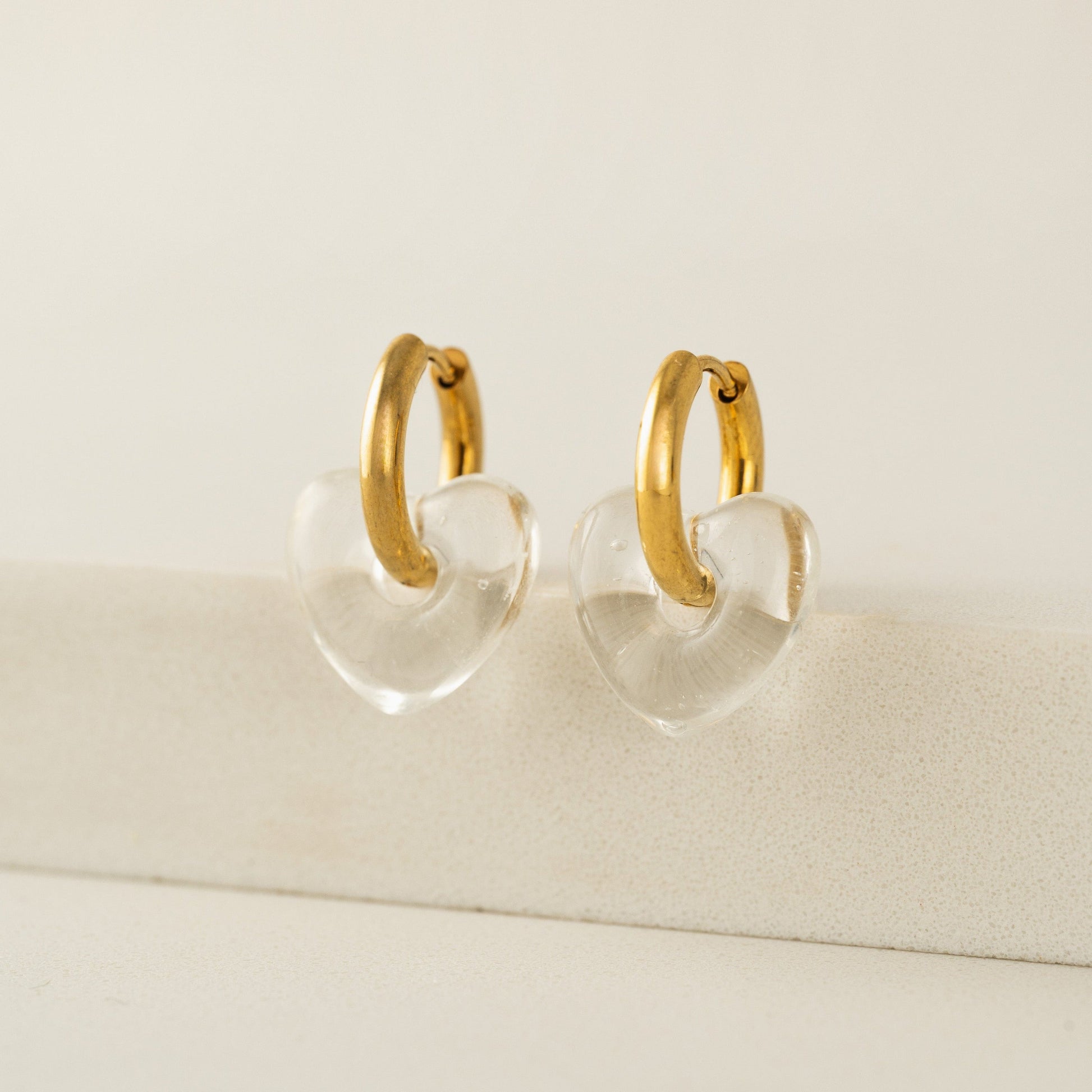 Gold hoop earrings with clear heart-shaped centers on a beige background
