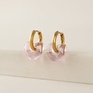 Gold hoop earrings with pink heart-shaped charms on a beige surface