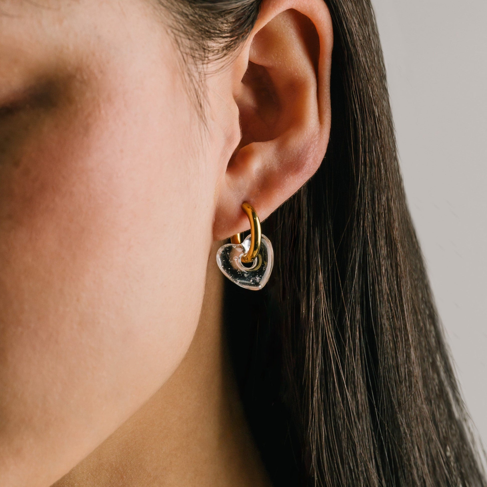 Close-up of an ear wearing a heart-shaped earring with a neutral background