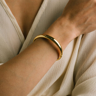 Gold bracelet on a wrist with a neutral background