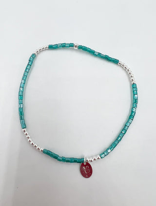 Turquoise beaded necklace with a red pendant on a light gray background