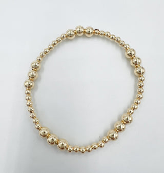 a gold beaded bracelet with different sized beads. 