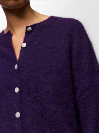 Close-up of a person wearing a fuzzy, deep purple button-up cardigan sweater with white buttons.