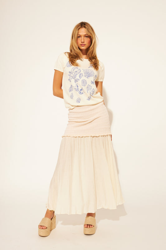 Woman wearing a pattern top and beige skirt on a white background