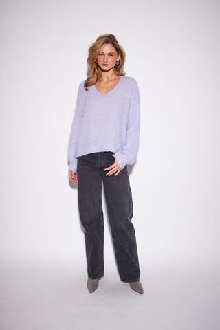 A woman modeling a light lavender knit sweater and dark gray wide-leg jeans against a plain white studio background.