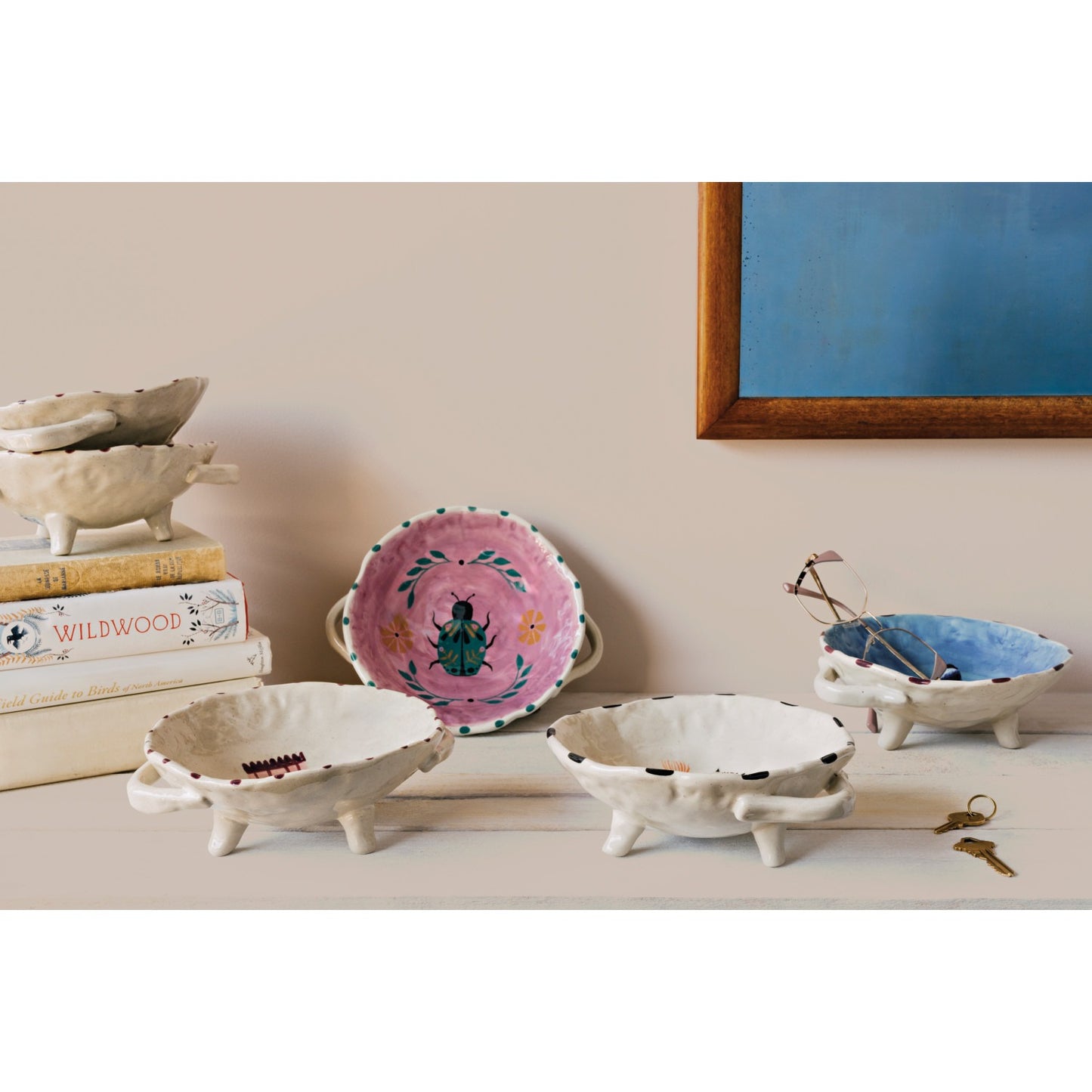 Collection of decorative ceramic bowls on a shelf with a painting in the background.