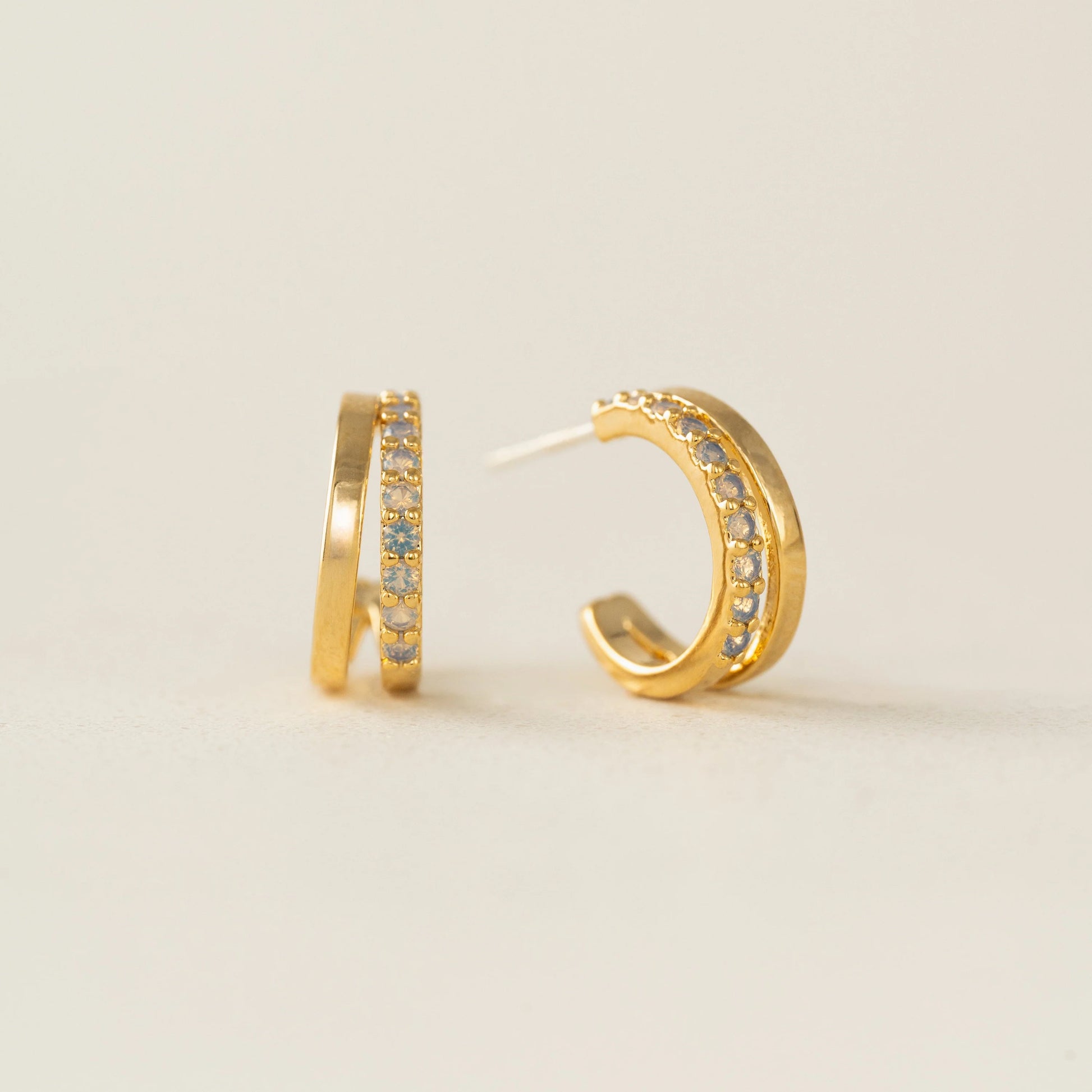 Gold hoop earrings with embedded stones on a light beige background