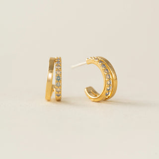 Gold hoop earrings with embedded stones on a light beige background
