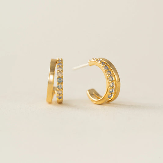 Gold hoop earrings with embedded stones on a light beige background