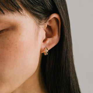 Close-up of an ear wearing a gold hoop earring with a neutral background
