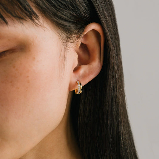Close-up of an ear wearing a gold hoop earring with a neutral background