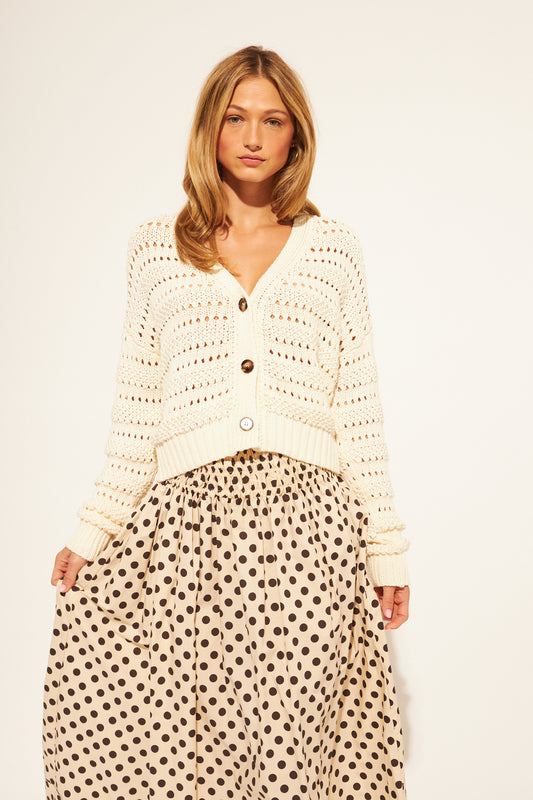 Woman wearing a cream crochet cardigan and polka dot skirt on a white background