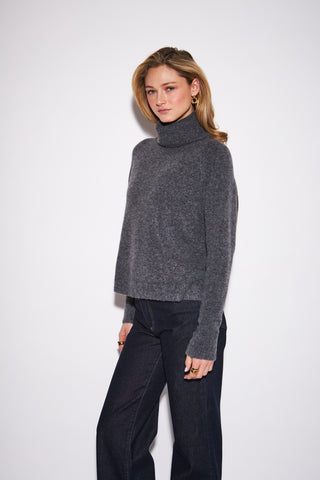 women wearing a charcoal sweater against a a neutral photo background. 