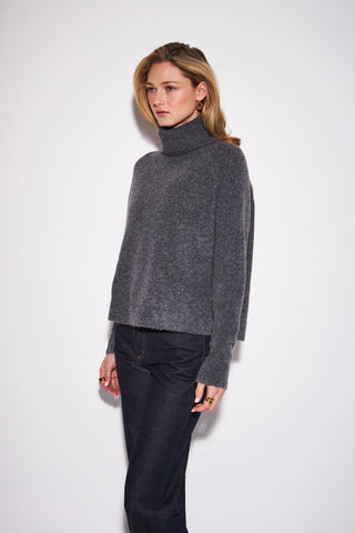 women wearing a charcoal sweater against a a neutral photo background. 