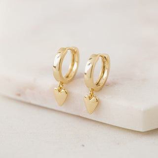 Gold hoop earrings with heart pendants on a light background
