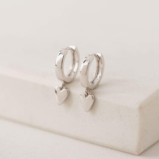 A pair of silver plated brass hoop earrings with heart-shaped charms, displayed on a card with 'LOVER'S TEMPO' branding.