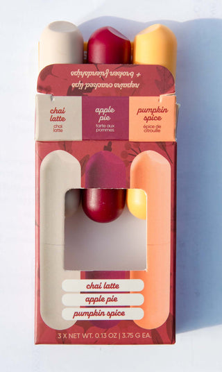 A boxed set of three lip balm tubes in red, burgundy, and yellow-orange packaging, with the flavors chai latte, apple pie, and pumpkin spice printed on the front.