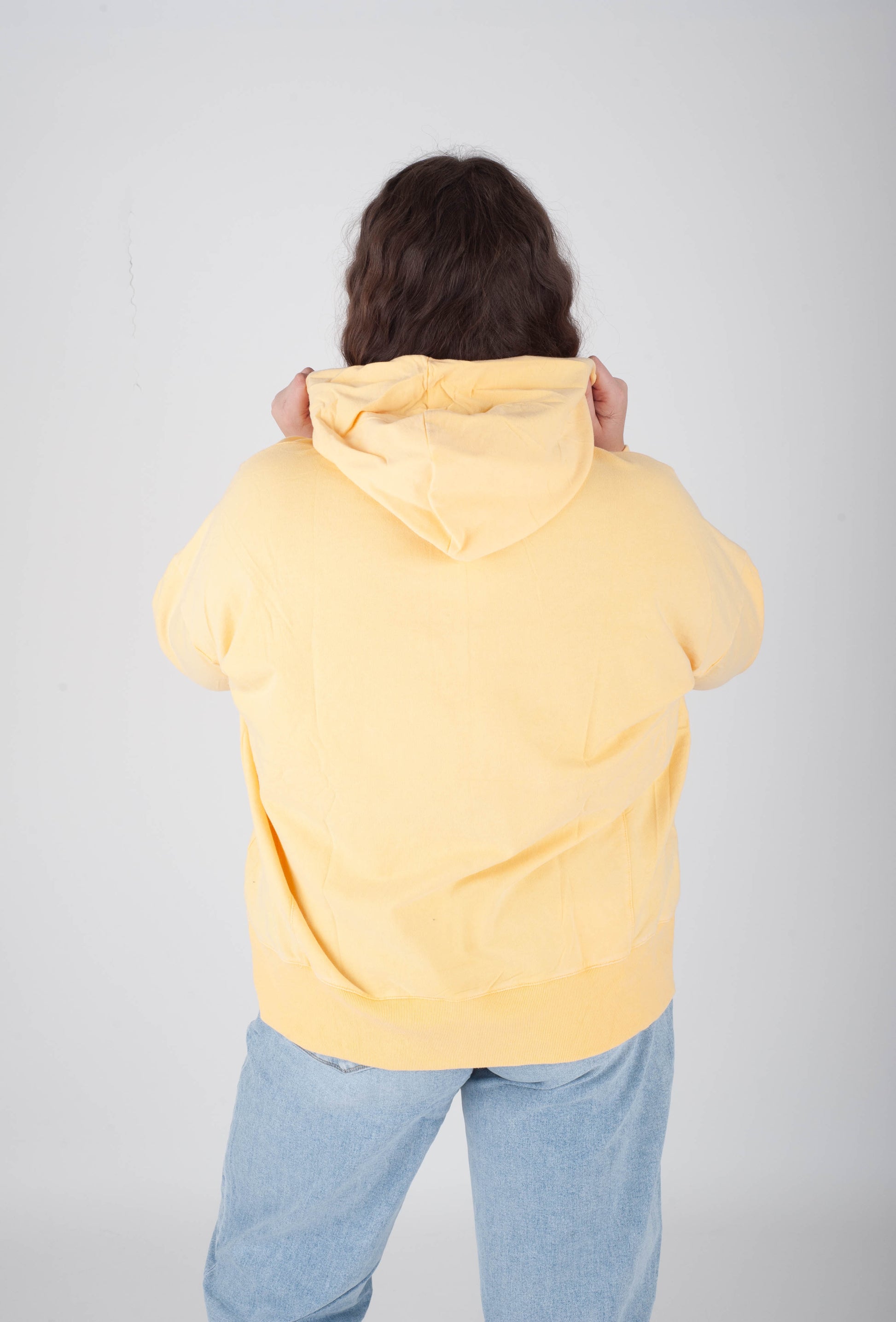 Person wearing a yellow hoodie and blue jeans on a plain background