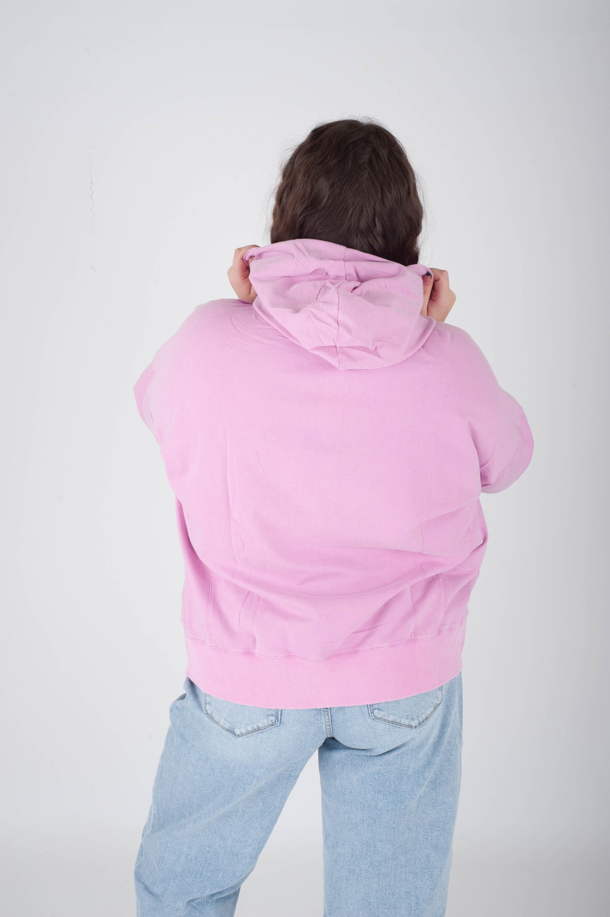 Person wearing a pink hoodie and light blue jeans on a white background