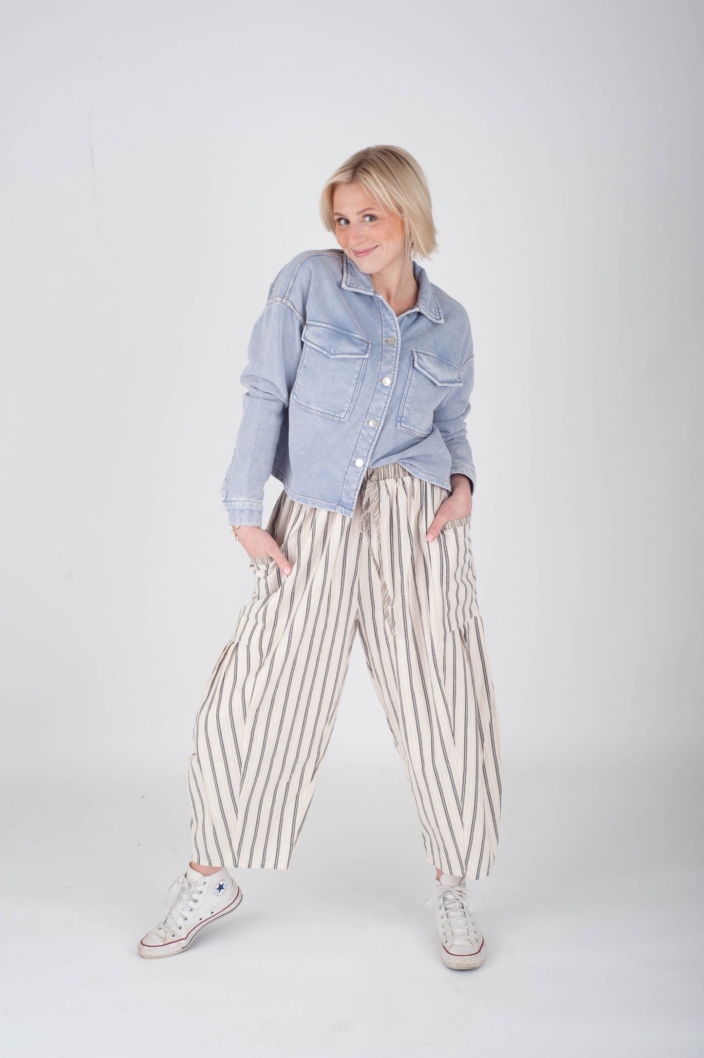 Person wearing a light blue denim shirt and striped pants on a white background