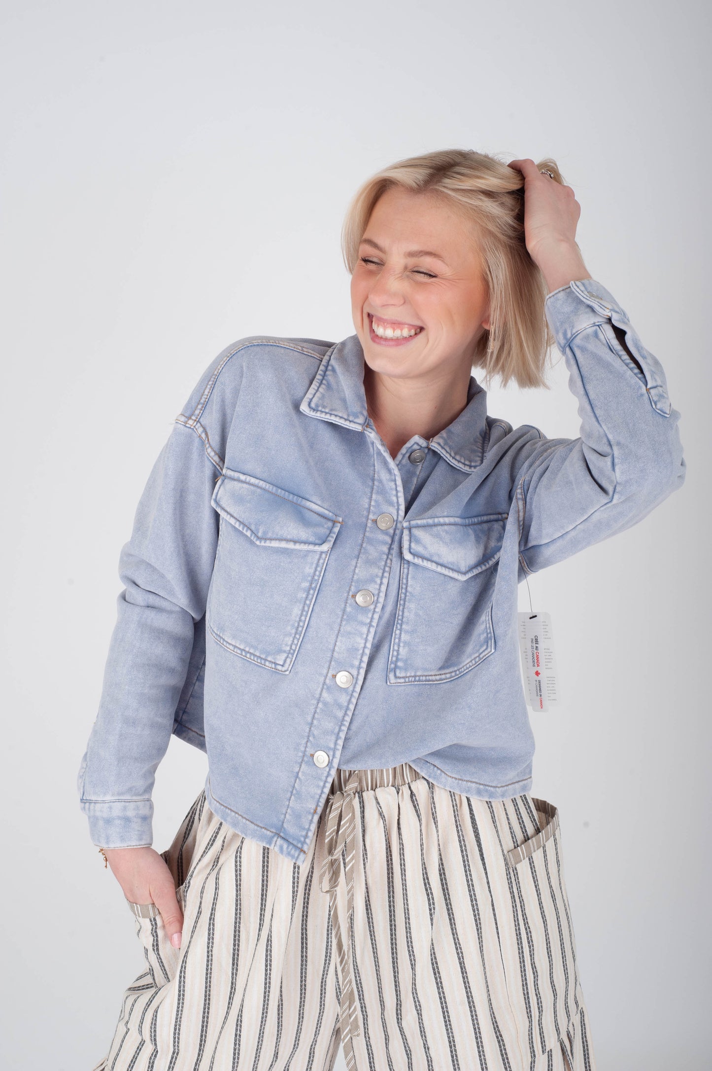 Woman wearing a light blue denim jacket and striped pants against a plain background