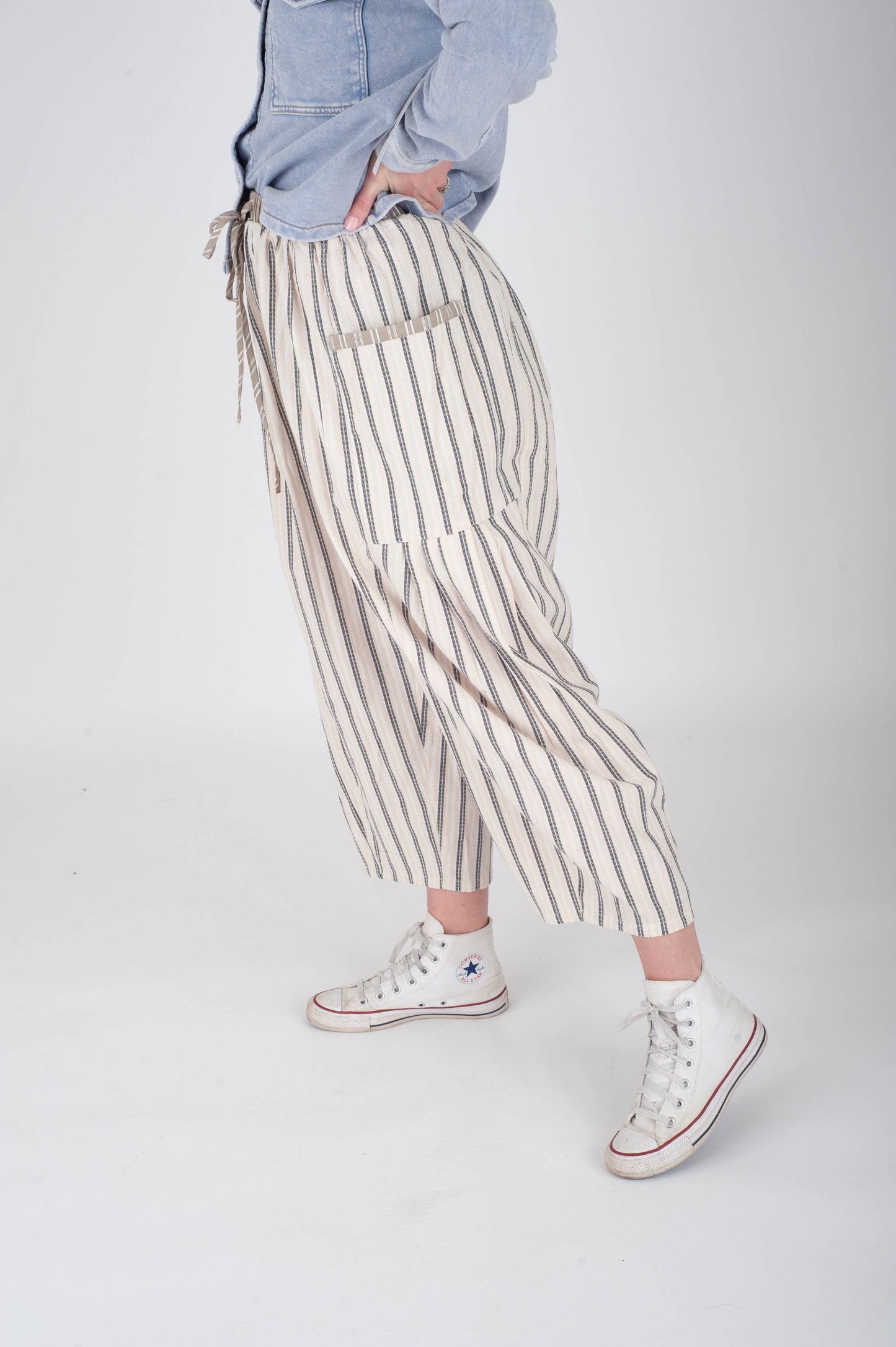 Person wearing striped pants and white sneakers on a plain background