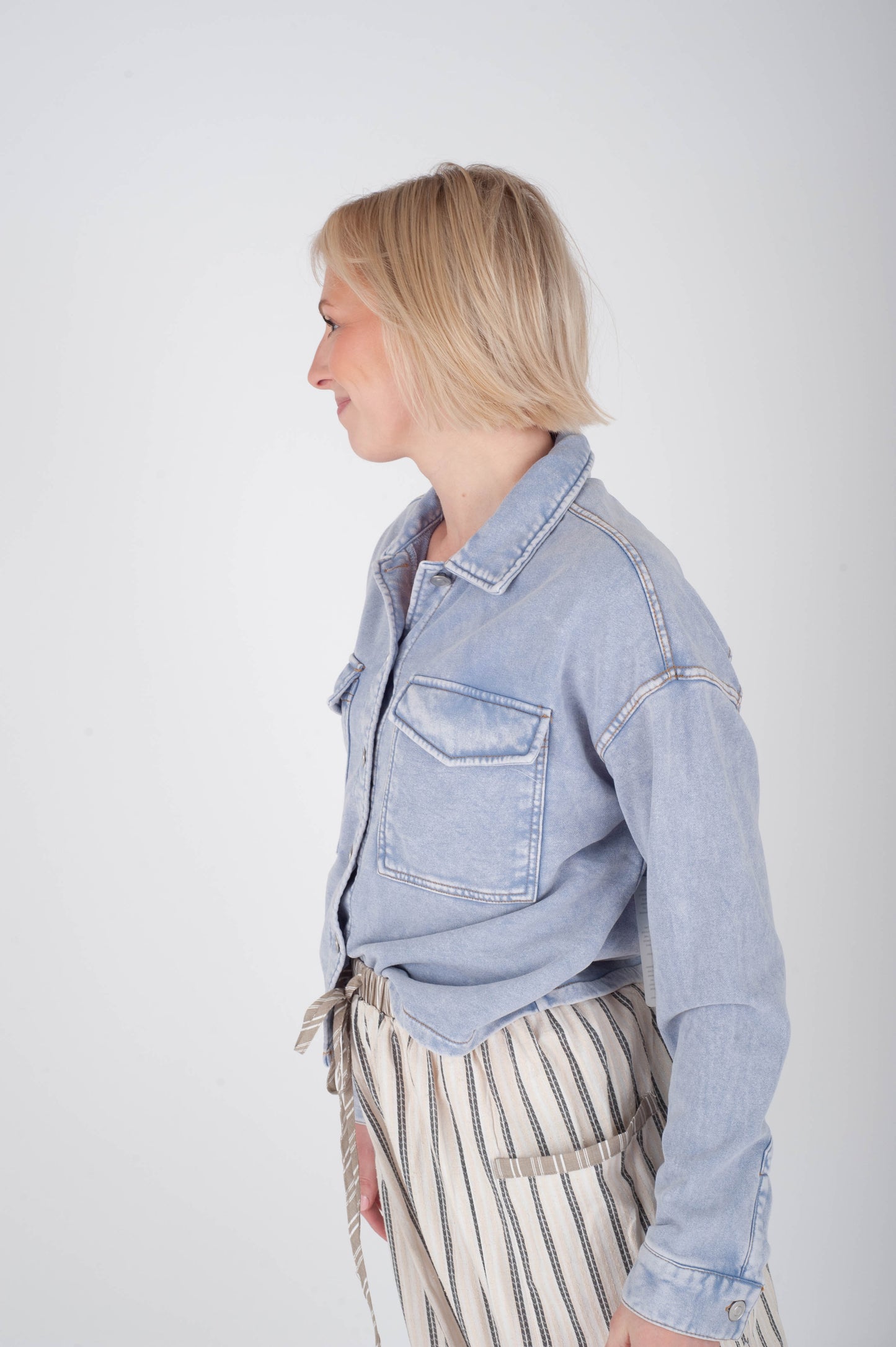 Person wearing a light blue denim jacket on a plain background
