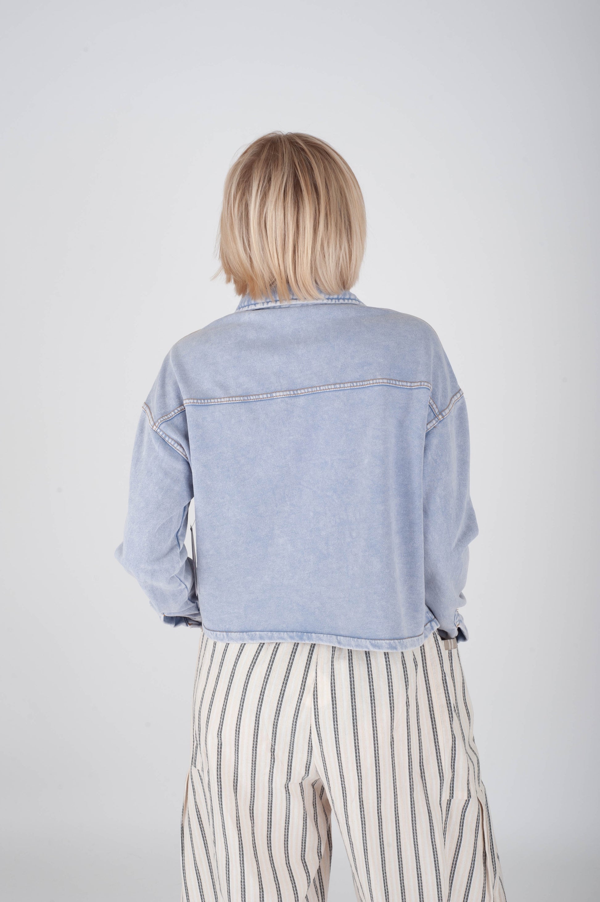 Person wearing a light blue denim jacket and striped pants on a plain background