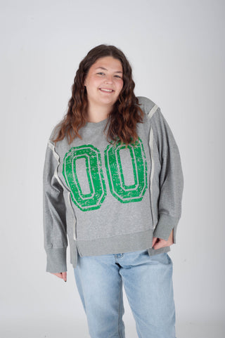 Person wearing a gray sweatshirt with green letters on a plain background