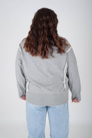 Person wearing a gray sweater with white accents on a plain background