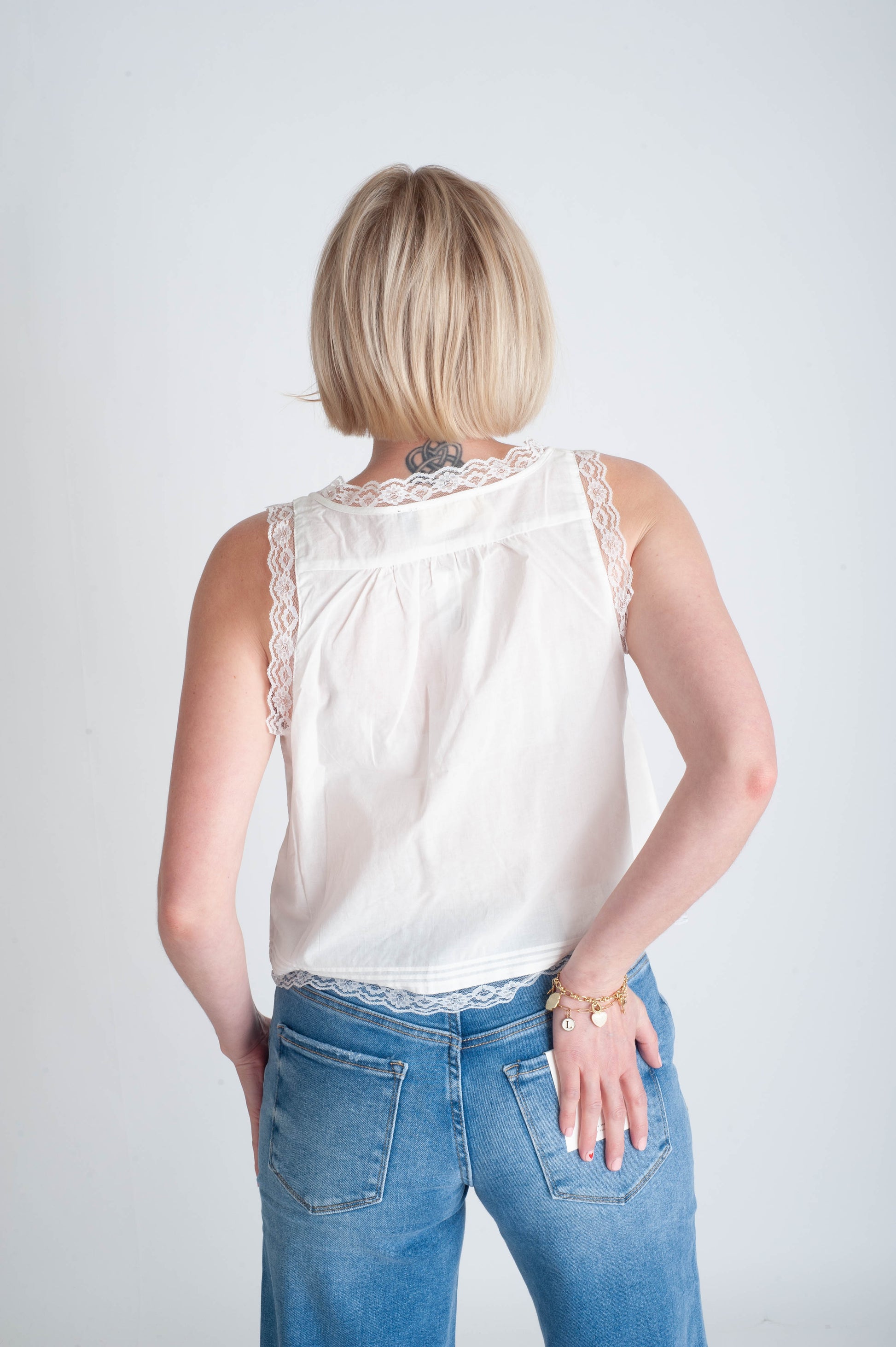 Person wearing a white sleeveless top with lace details and blue jeans on a plain background
